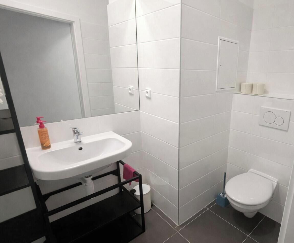 Un baño con lavamanos blanco, espejo, inodoro y zona de ducha.