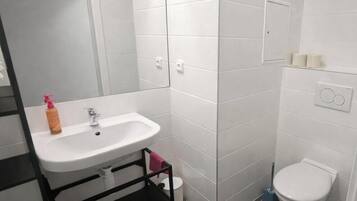 Un baño con lavamanos blanco, espejo, inodoro y zona de ducha.