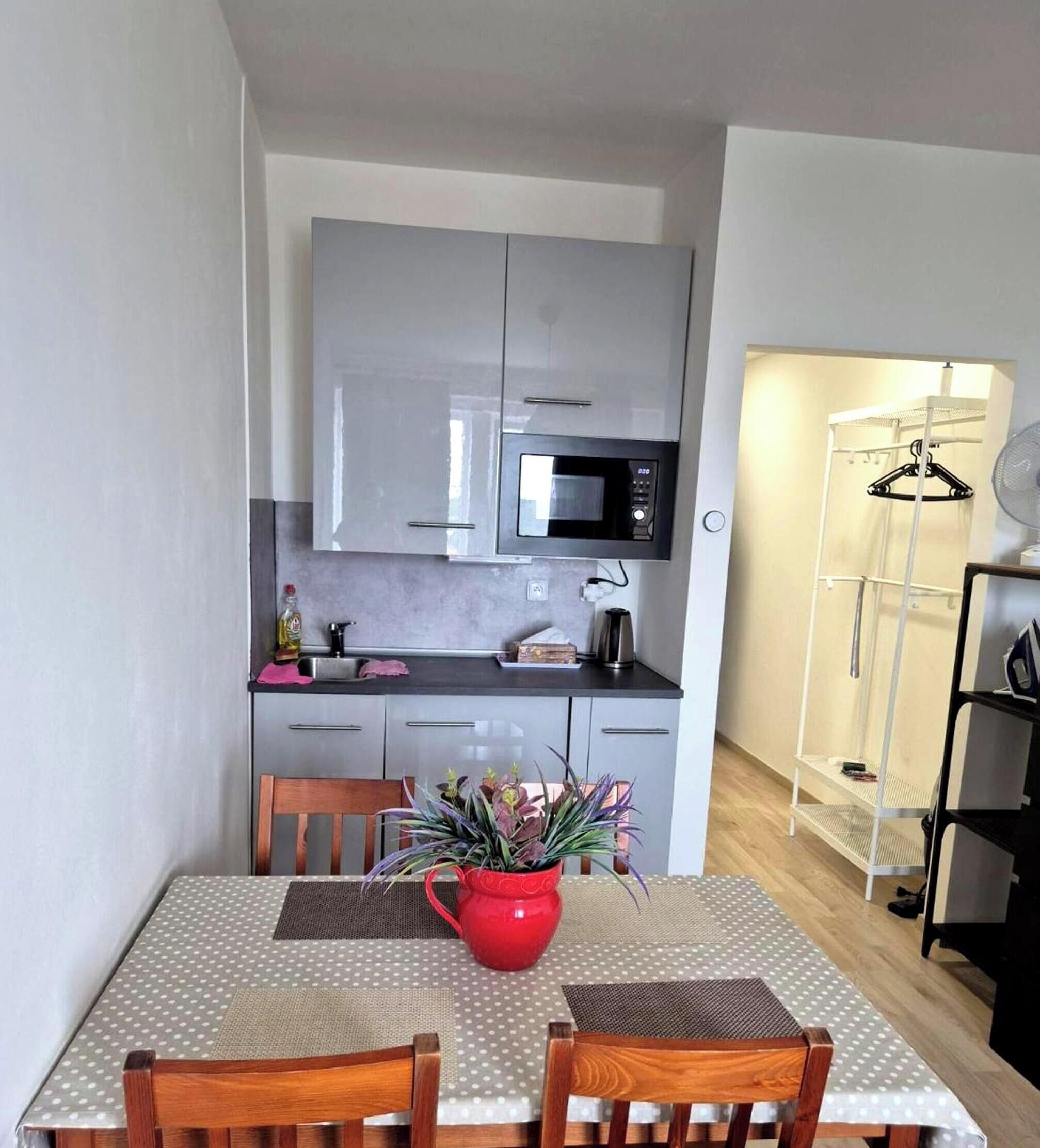 Cozinha compacta com micro-ondas, pia e armários. Há uma mesa de jantar com cadeiras e uma panela vermelha em cima.