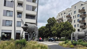 Un bâtiment moderne doté de balcons, une zone piétonne agrémentée d’une sculpture et une vitrine.