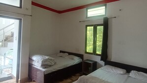 Un dormitorio con dos camas, un ventilador de techo, una ventana con cortinas verdes y vistas al exterior.