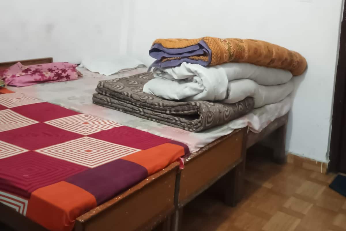 Une petite chambre avec un lit simple, un plancher en bois, un ventilateur de plafond et un lit recouvert d’une courtepointe à motifs et agrémenté d’oreillers.