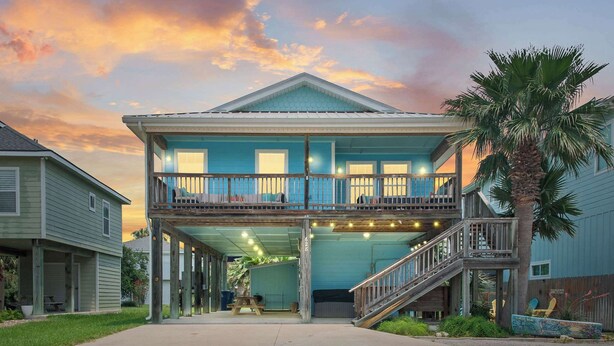 A two-story house with a balcony, a covered porch, and a staircase leading to the upper level. - Cozy 3bdr Sleeps 8 (Port Aransas)