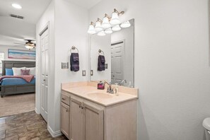 Un baño con tocador color beige, un espejo grande y un ventilador de techo.