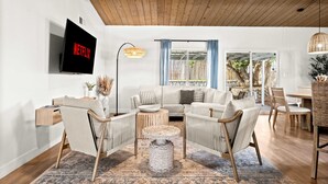 A modern living room with a flat-screen TV, a sofa, chairs, a coffee table, and a dining area with a table and chairs.