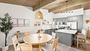 A modern kitchen with grey cabinets, a central island, and a dining area with a round table and chairs.