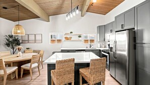 A modern kitchen with a central island, wooden ceiling beams, and stainless steel appliances.
