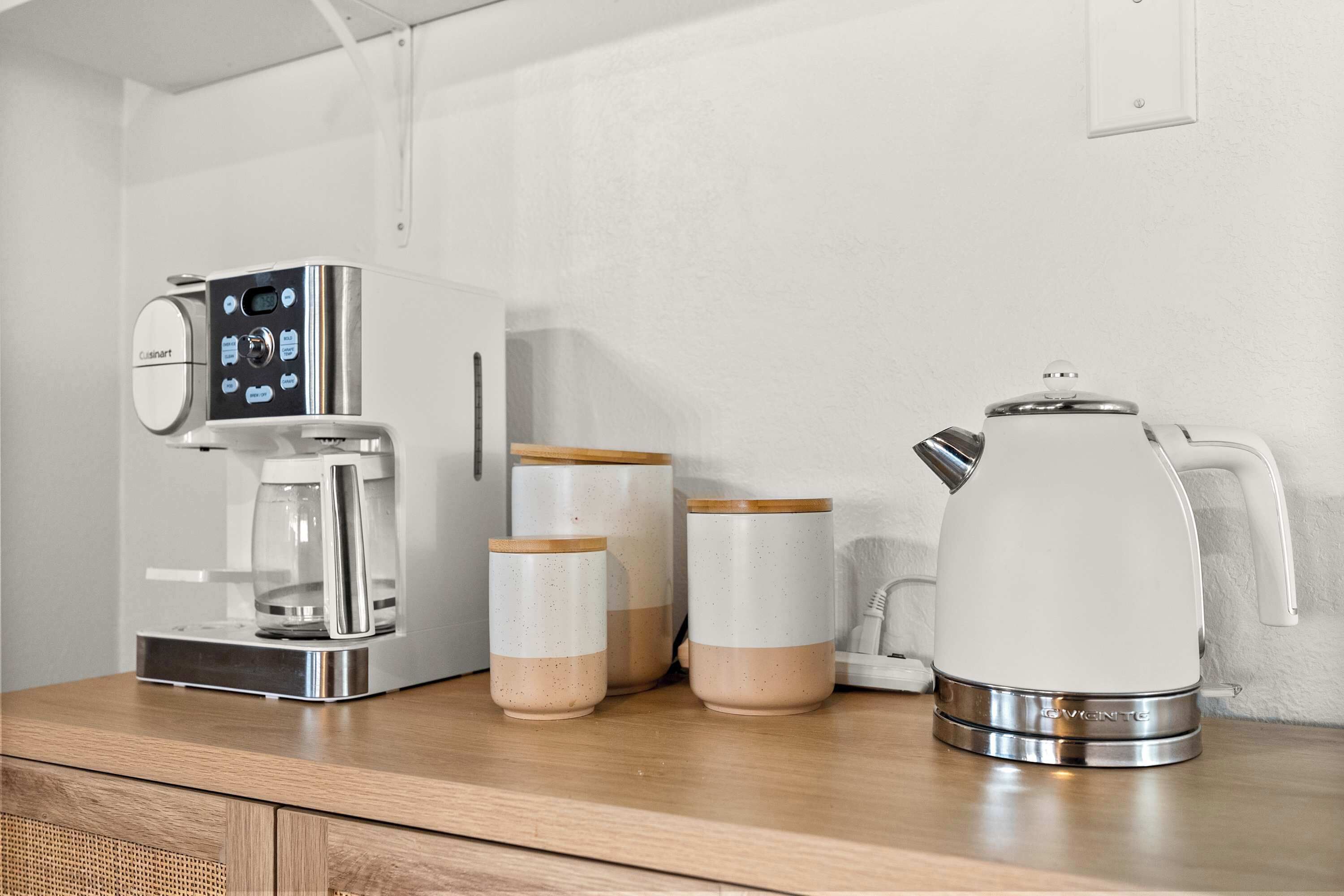 A kitchen with a coffee maker, two jars, and a teapot.