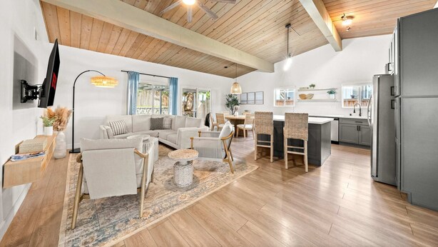 A spacious living area with a wooden ceiling, a sofa set, a dining table, and a kitchen with a refrigerator.