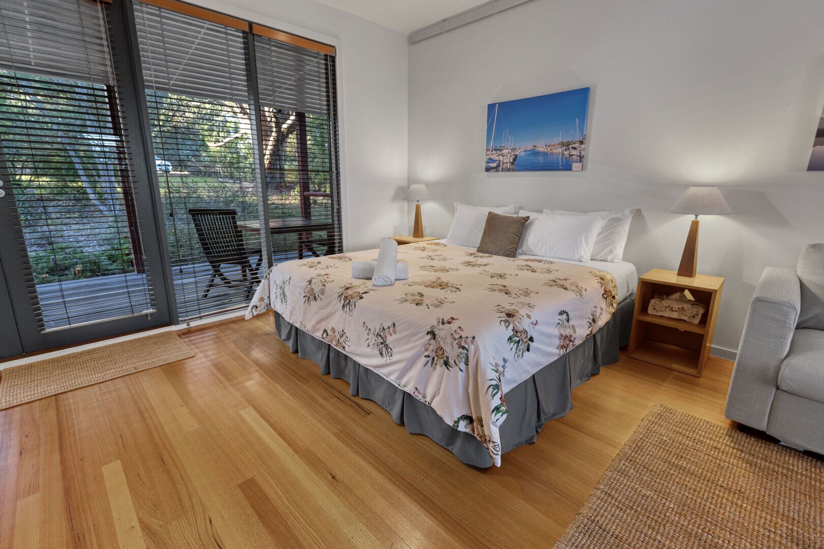 Un dormitorio con una cama, una mesita de noche, una silla, una ventana con persianas y un cuadro en la pared.