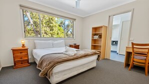 Une chambre à coucher comprenant un lit, une table de chevet avec une lampe, une chaise en bois et une étagère intégrée.