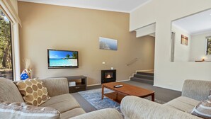 Un salon comprenant un ensemble de canapés, un téléviseur à écran plat, une cheminée et un escalier.