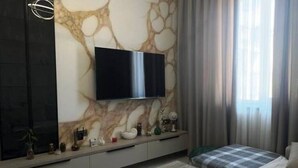 A modern bedroom with a flat-screen TV mounted on a marble wall, a bed with a striped bedspread, and a bedside table with decorative items.
