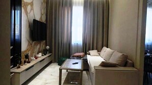A modern living room with a sofa, a coffee table, a TV mounted on the wall, and a window with curtains.