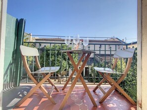 A balcony with a table and two chairs, a green fence, and a building in the background.