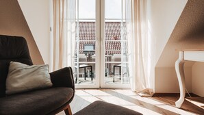 A room with a sofa, a table, and a view through a glass door to an outdoor area with a tiled roof. - Apartment 'Shenandoah' with Private Balcony, Shared Garden and Wi-Fi (Baltrum)