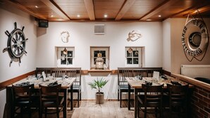 A restaurant with wooden tables and chairs, a ship's wheel, and a U.S. Navy lifebuoy on the wall. - Apartment 'Shenandoah' with Private Balcony, Shared Garden and Wi-Fi (Baltrum)