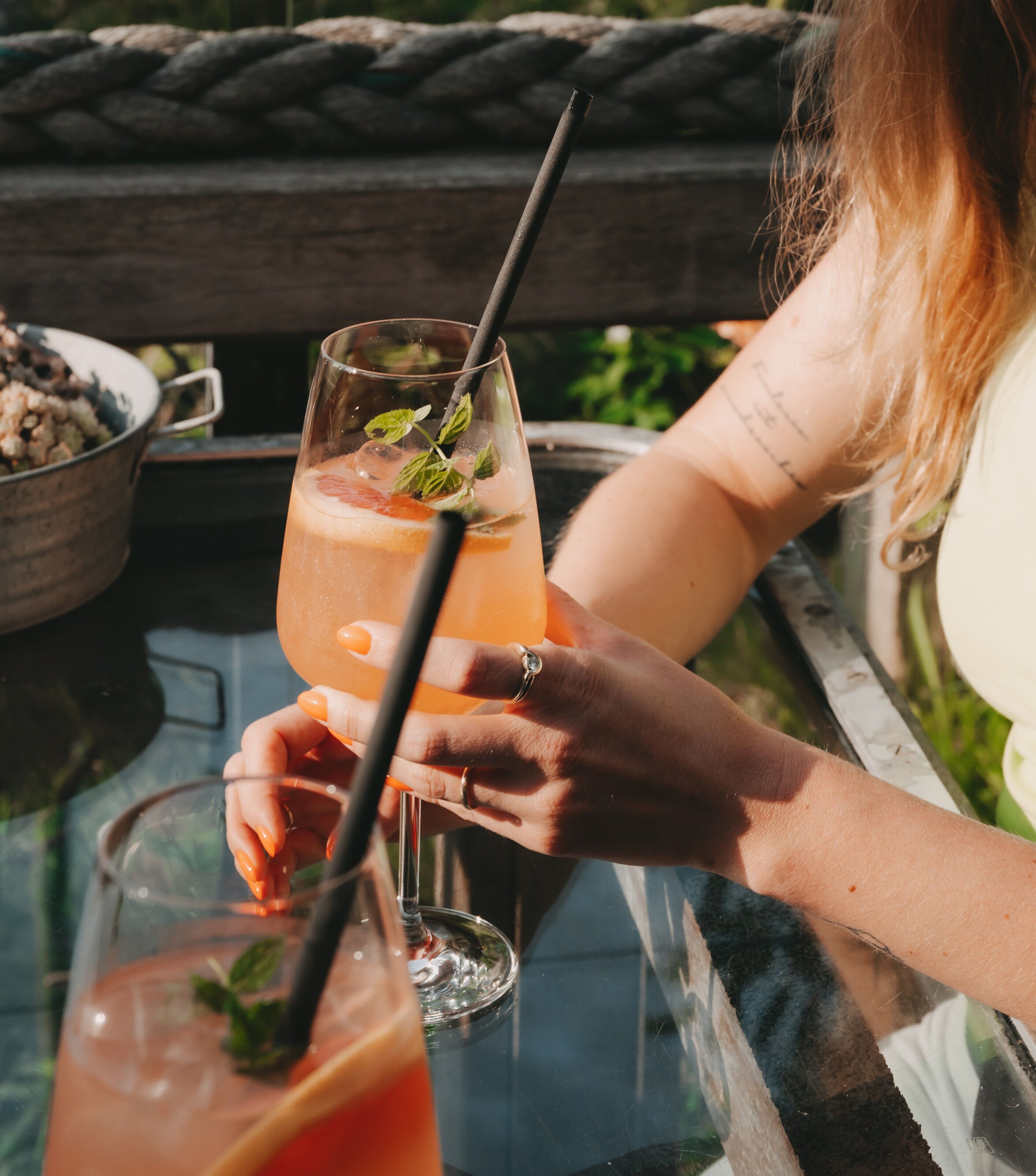 A person holding a glass with a straw, another glass with a drink, and a bowl of food on a table.