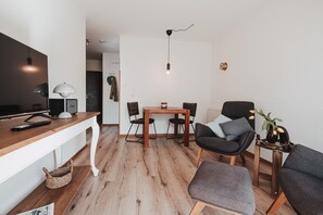Un salon moderne avec une table en bois, deux chaises, un canapé, un téléviseur et une lampe.