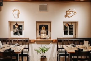 Um restaurante com mesas e cadeiras de madeira, e um vaso de planta no centro.