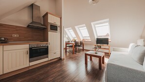 A modern kitchen with wooden cabinets, a built-in oven, and a microwave. There is a dining area with a table and chairs, and a living room with a sofa and a TV. - Apartment 'Lord Nelson' with Shared Terrace, Shared Garden and Wi-Fi (Baltrum)