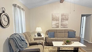 Un salon avec un canapé, une table basse, un tapis, une horloge et deux tableaux accrochés au mur.