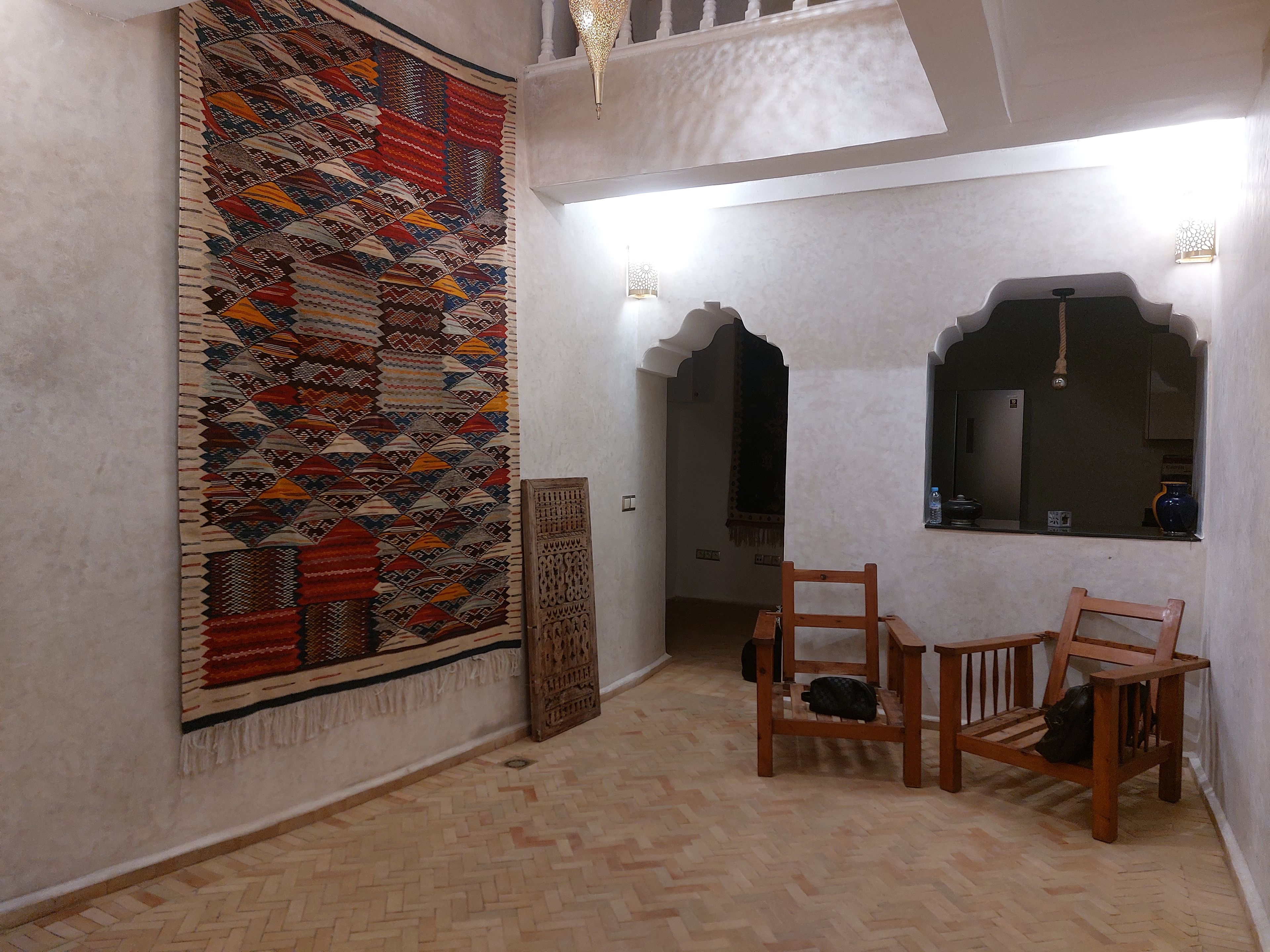 Une pièce avec un tapis à motifs, des chaises en bois, une petite table et un miroir décoratif.