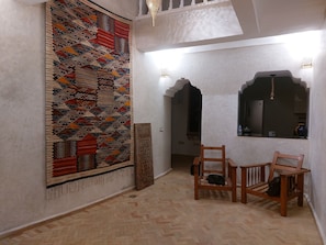 A room with a patterned carpet, wooden chairs, a small table, and a decorative mirror.