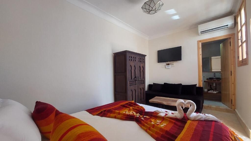 A hotel room with a bed, a wooden wardrobe, a flat-screen TV, and a desk with a chair.