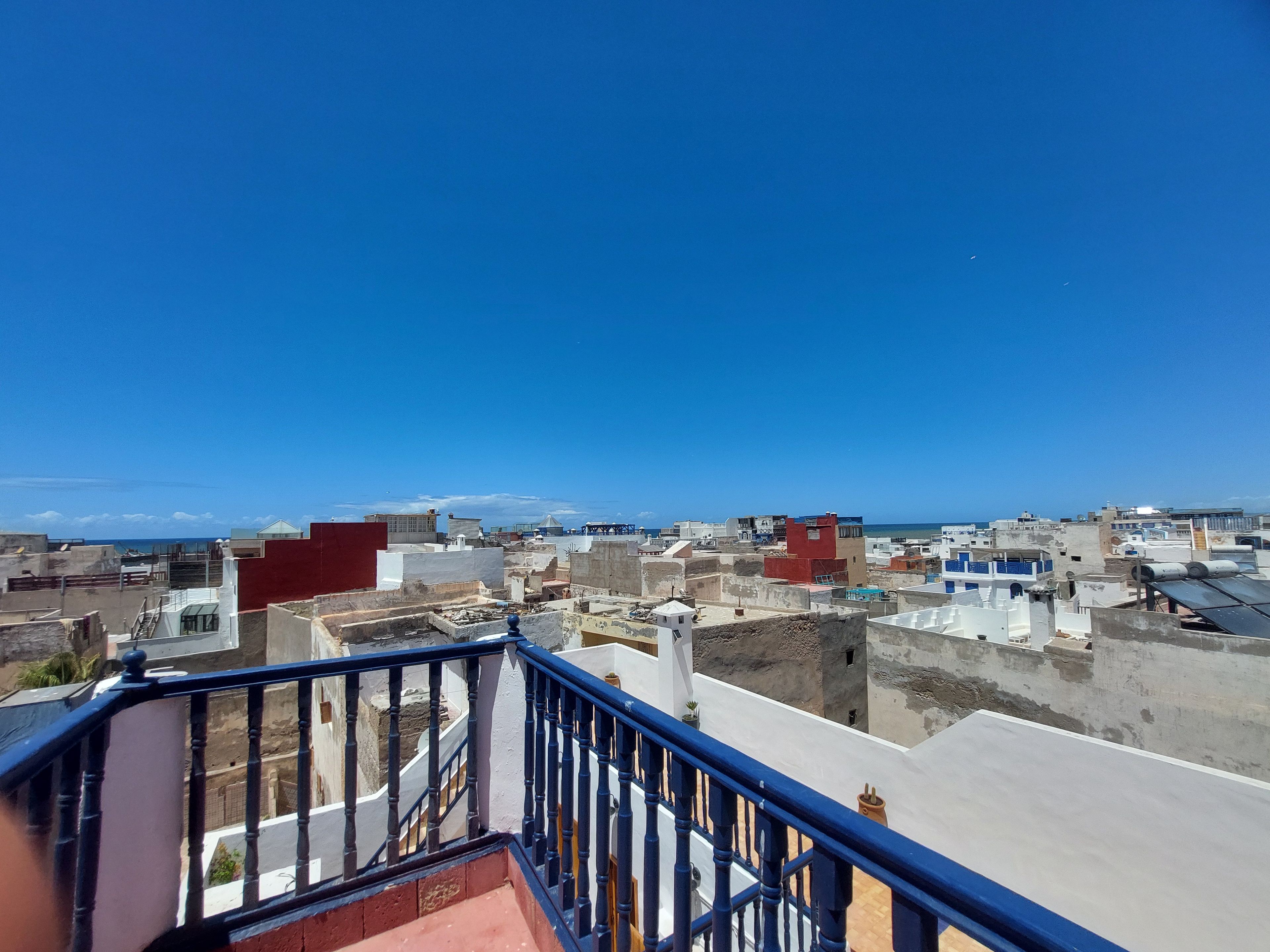 Une vue urbaine avec un ciel bleu dégagé, une variété de styles architecturaux et une rampe d’escalier bleue bien visible.