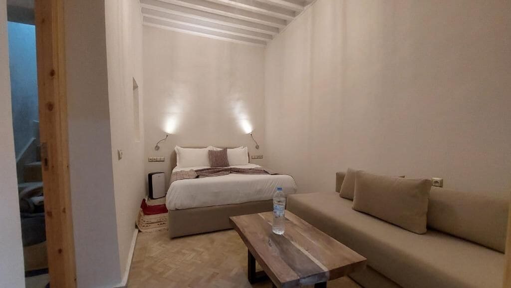 Een kamer met een bed, een slaapbank, een houten salontafel en een kleine tafel met een fles.