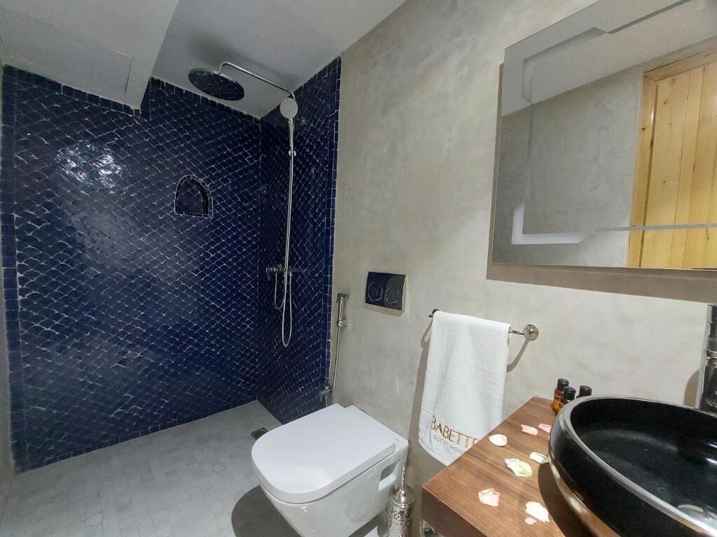 Een badkamer met een wit toilet, een zwarte wastafel, een spiegel en een douchegedeelte met blauwe tegels.