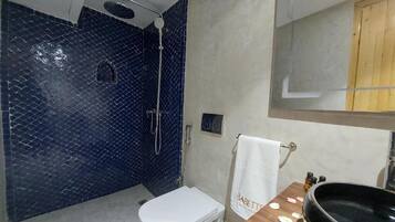 Een badkamer met een wit toilet, een zwarte wastafel, een spiegel en een douchegedeelte met blauwe tegels.