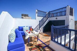 A rooftop terrace with a blue sofa set, a table with drinks, and a staircase. - Riad Babette (Essaouira)