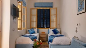 A small, cozy room with two beds, a television, a window with shutters, and a framed picture on the wall. - Riad Babette (Essaouira)