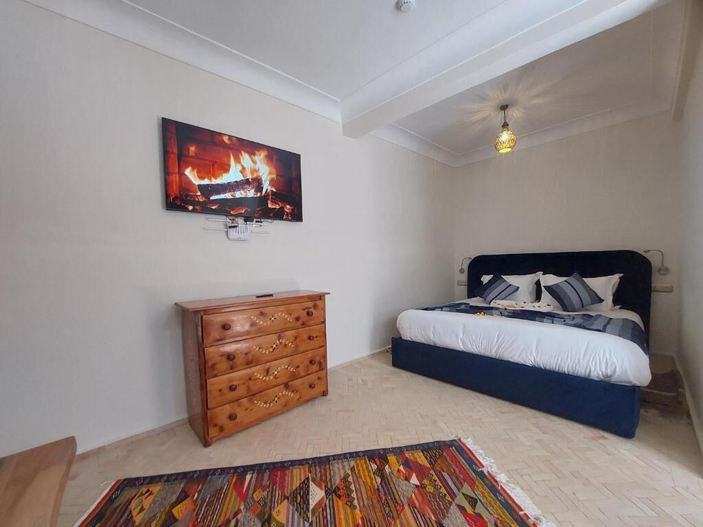 Een slaapkamer met een bed, een houten dressoir, een tv aan de muur en een plafondlamp.
