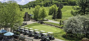 A golf course with a clubhouse, a parking area with golf carts, and surrounding greenery.