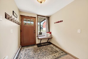 A hallway with a wooden door, a bench with a cushion, a coat rack, and a view of a red building outside. - Across from Holiday Valley, 2 King Beds (Ellicottville)