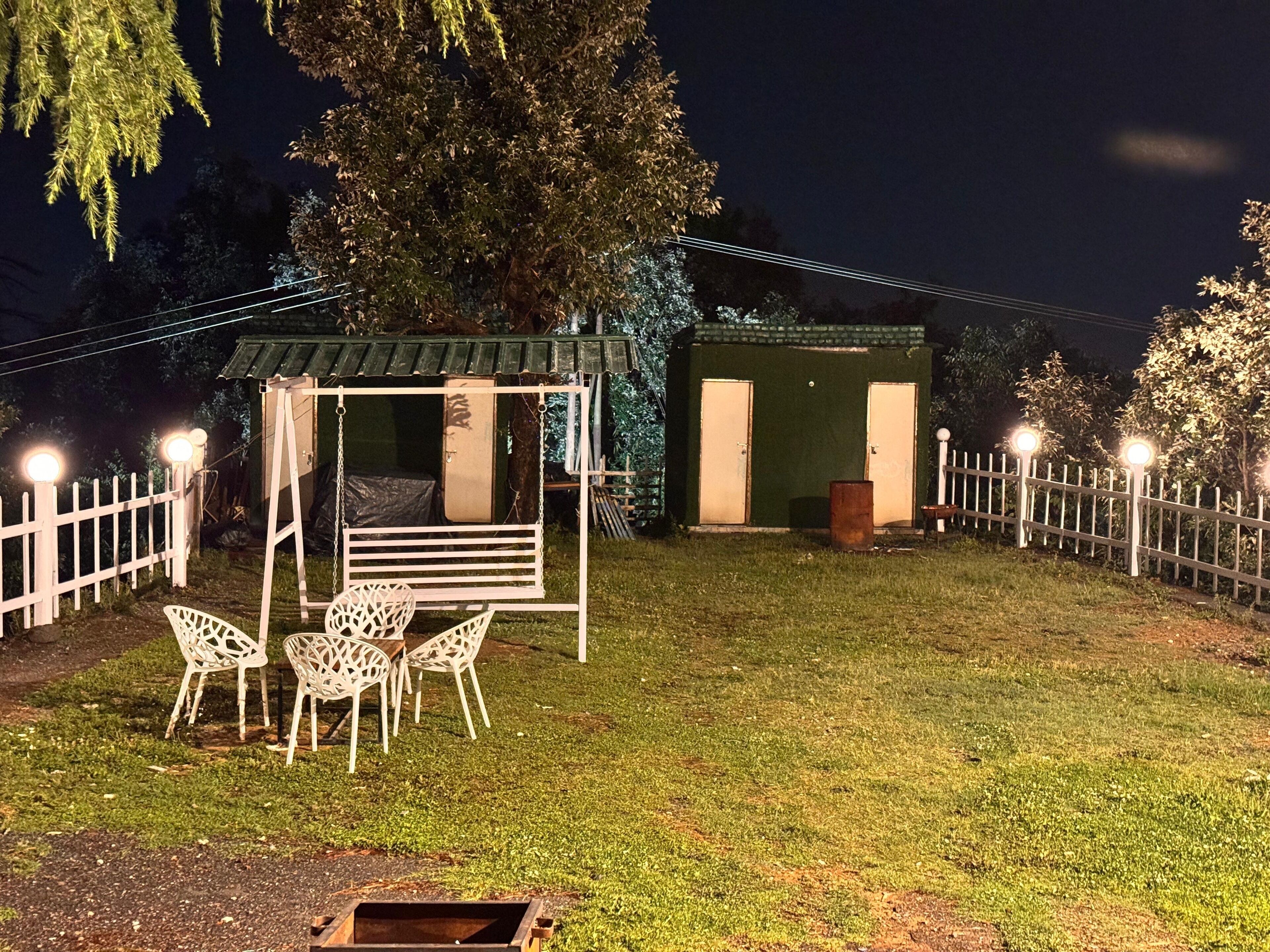 A gazebo with a swing, surrounded by a white fence, and a small shed in the background.
