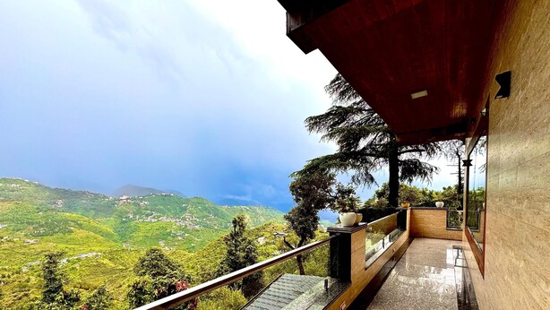 A balcony with a view of green hills and a cloudy sky. - Heavens View Resort (Mussoorie)