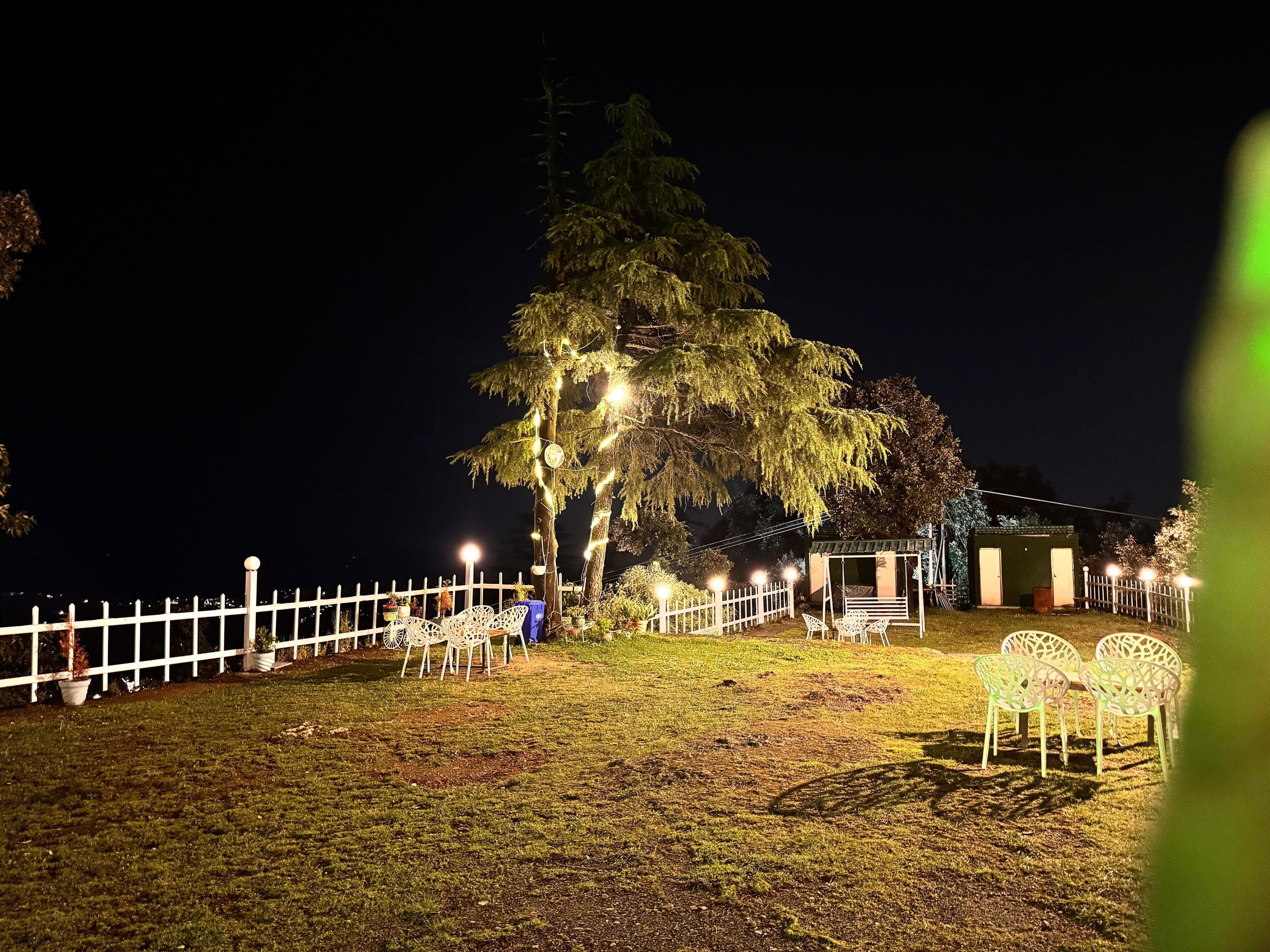 A nighttime outdoor area with a white fence, a swing set, and a small building.