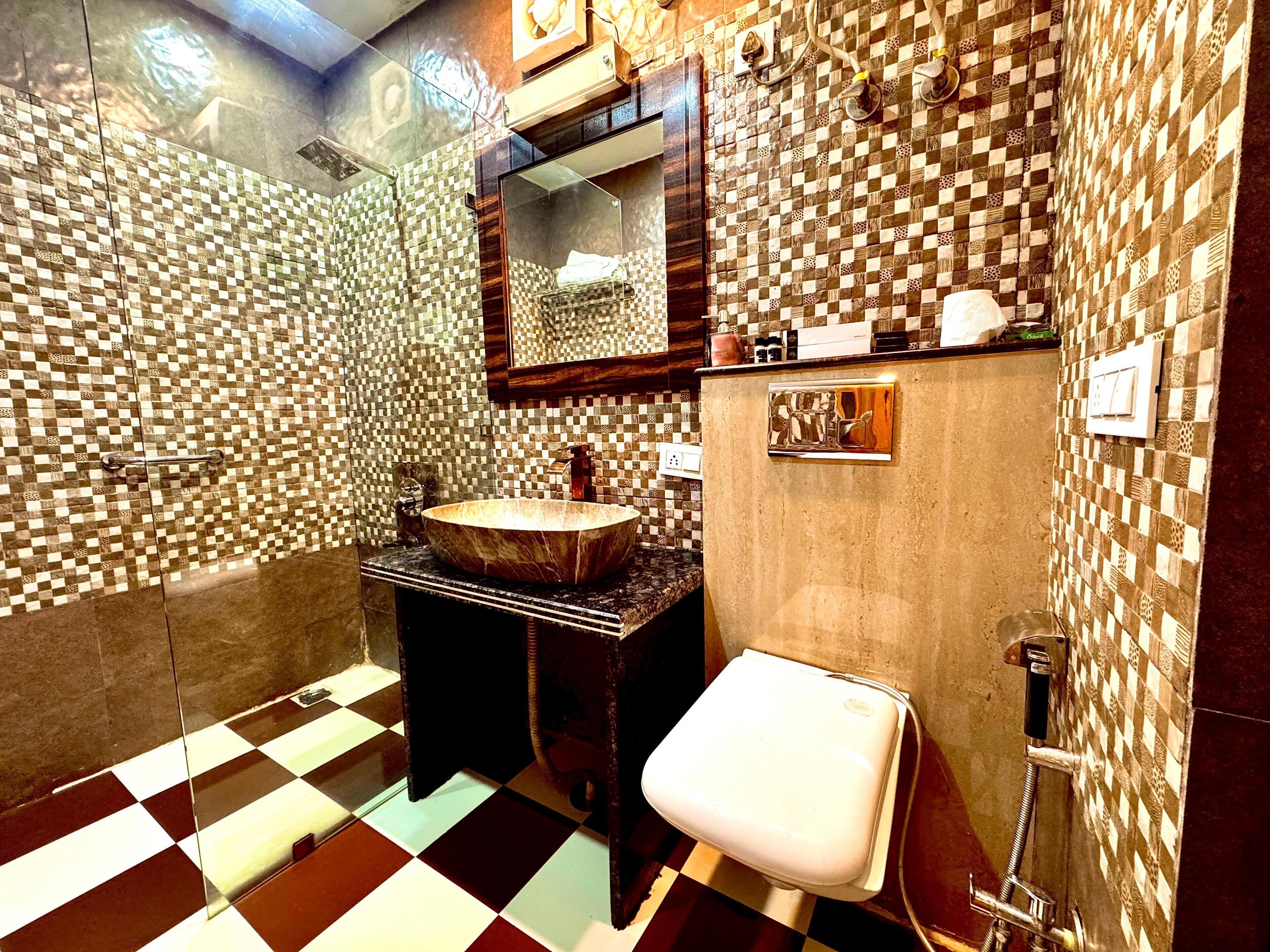 A bathroom with a checkered floor, a wooden vanity with a vessel sink, a mirror above the sink, and a toilet with a shower attachment.