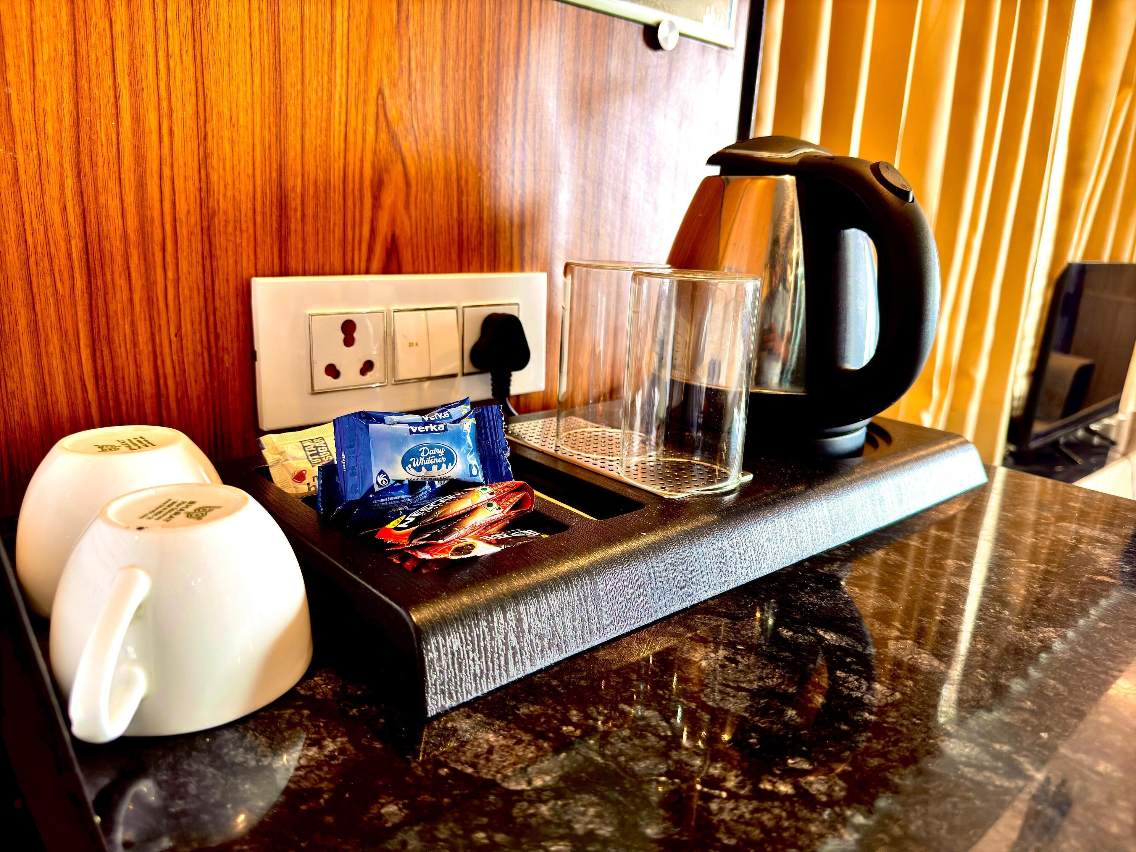 Eine Küchenarbeitsplatte mit einer Kaffeemaschine, zwei weißen Tassen, einem Glas und einer Tüte Snacks.