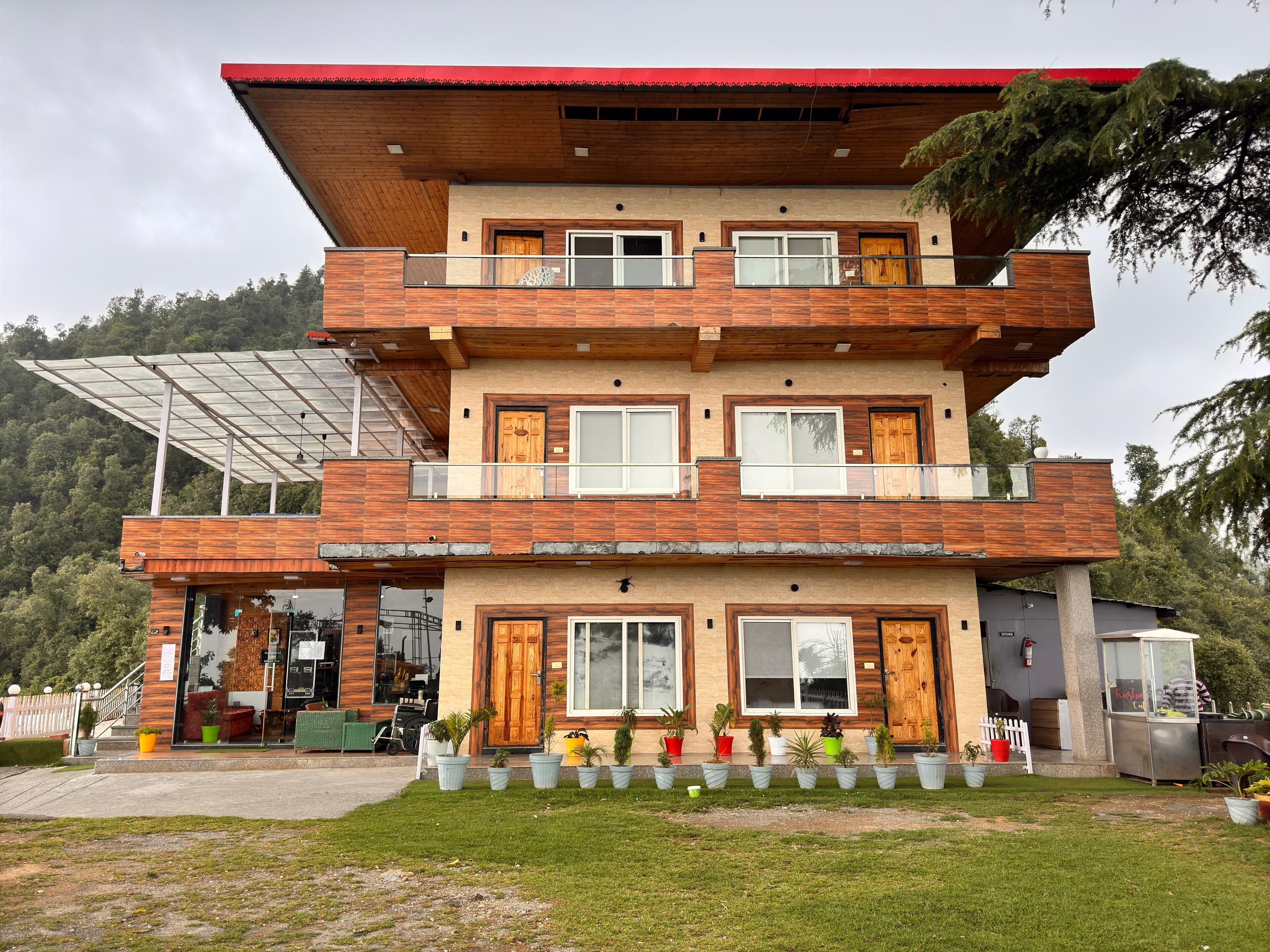 Un edificio de varios pisos con diseño moderno, que cuenta con balcones, ventanas amplias y una variedad de plantas en macetas en el jardín delantero.