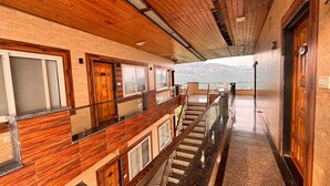 A hotel corridor with wooden paneling, a glass railing, and a view of a mountainous landscape. - Heavens View Resort (Mussoorie)