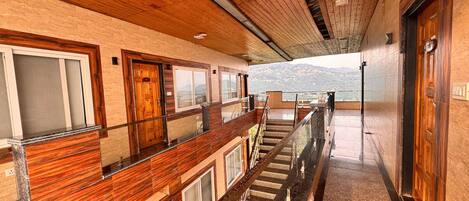 A hotel corridor with wooden paneling, a glass railing, and a view of a mountainous landscape.