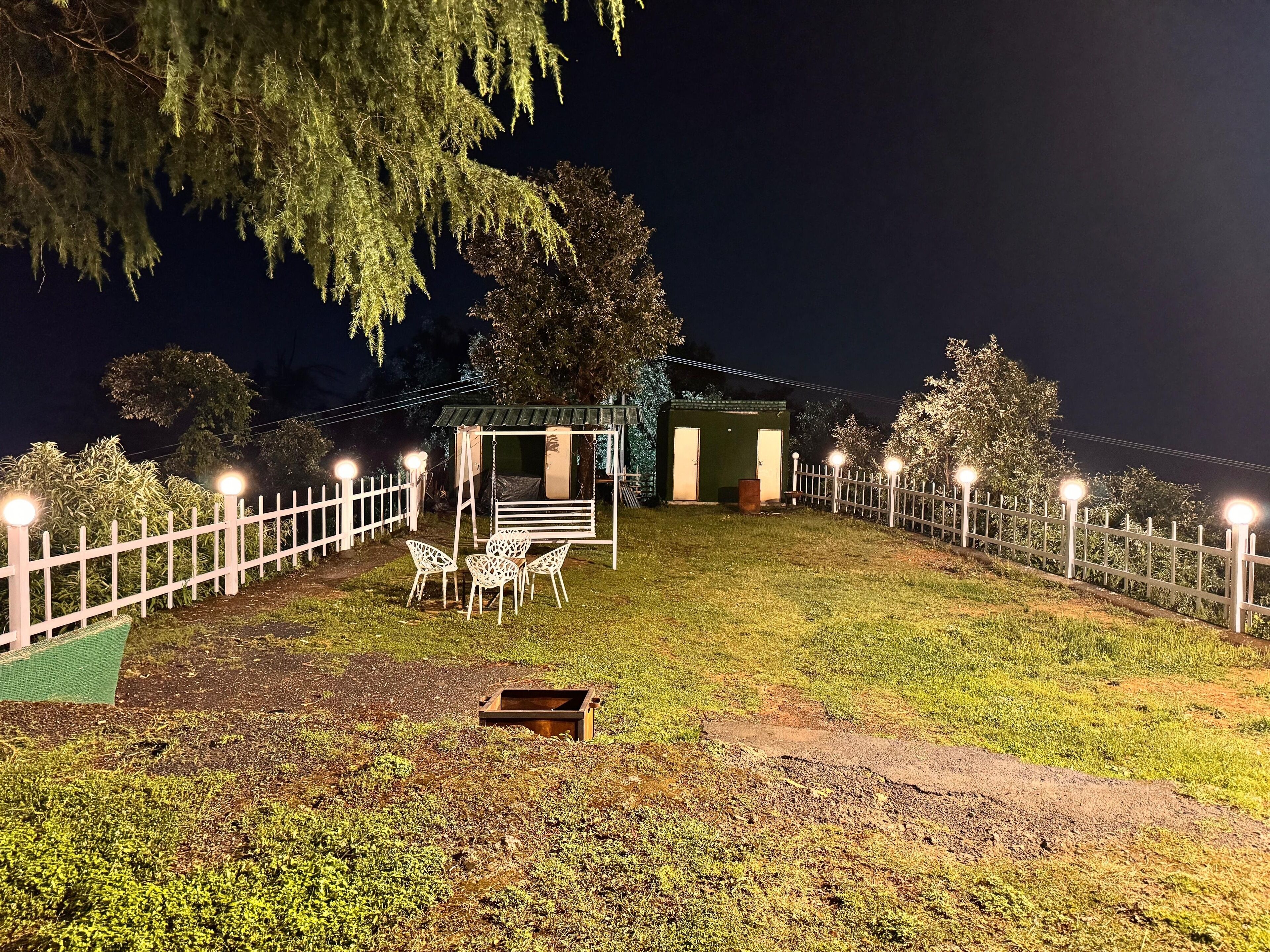 A well-lit outdoor area with a swing set, a small shed, and a white picket fence.
