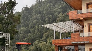A modern building with a red roof, a glass conservatory, and a view of a forested hill. - Heavens View Resort (Mussoorie)