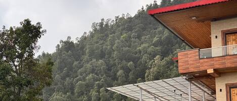 Un edificio moderno con techo rojo, una estructura de cristal y vistas a una colina boscosa.