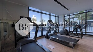 Une salle de sport moderne dotée de grandes fenêtres, de tapis de course et d’un mur entièrement recouvert de miroirs.